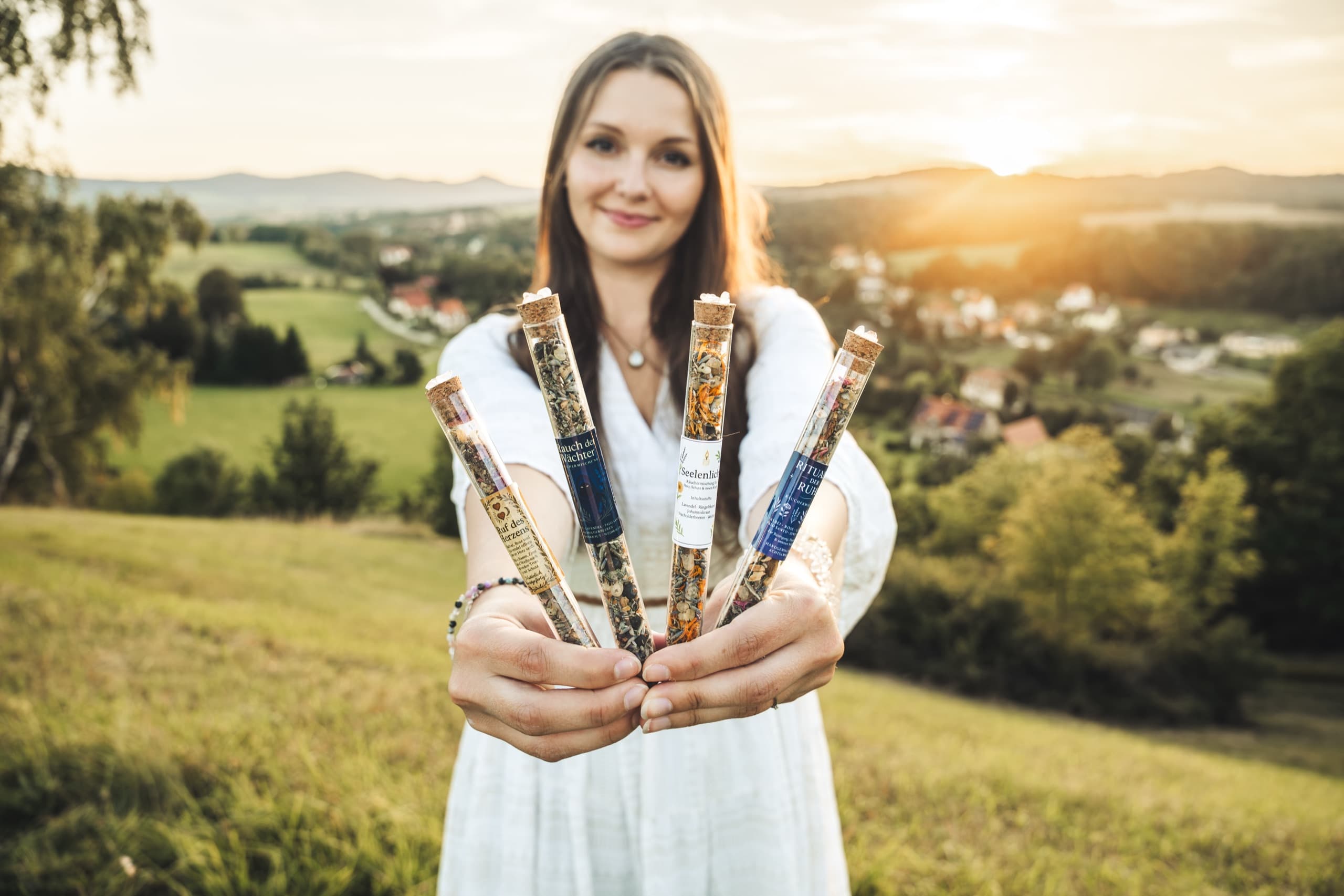 Linda hält die vier einzigartigen Seelenzauber Räuchermischungen in den Händen, umgeben von einem magischen Glanz, der die Essenz der Natur und des Wohlbefindens einfängt.s